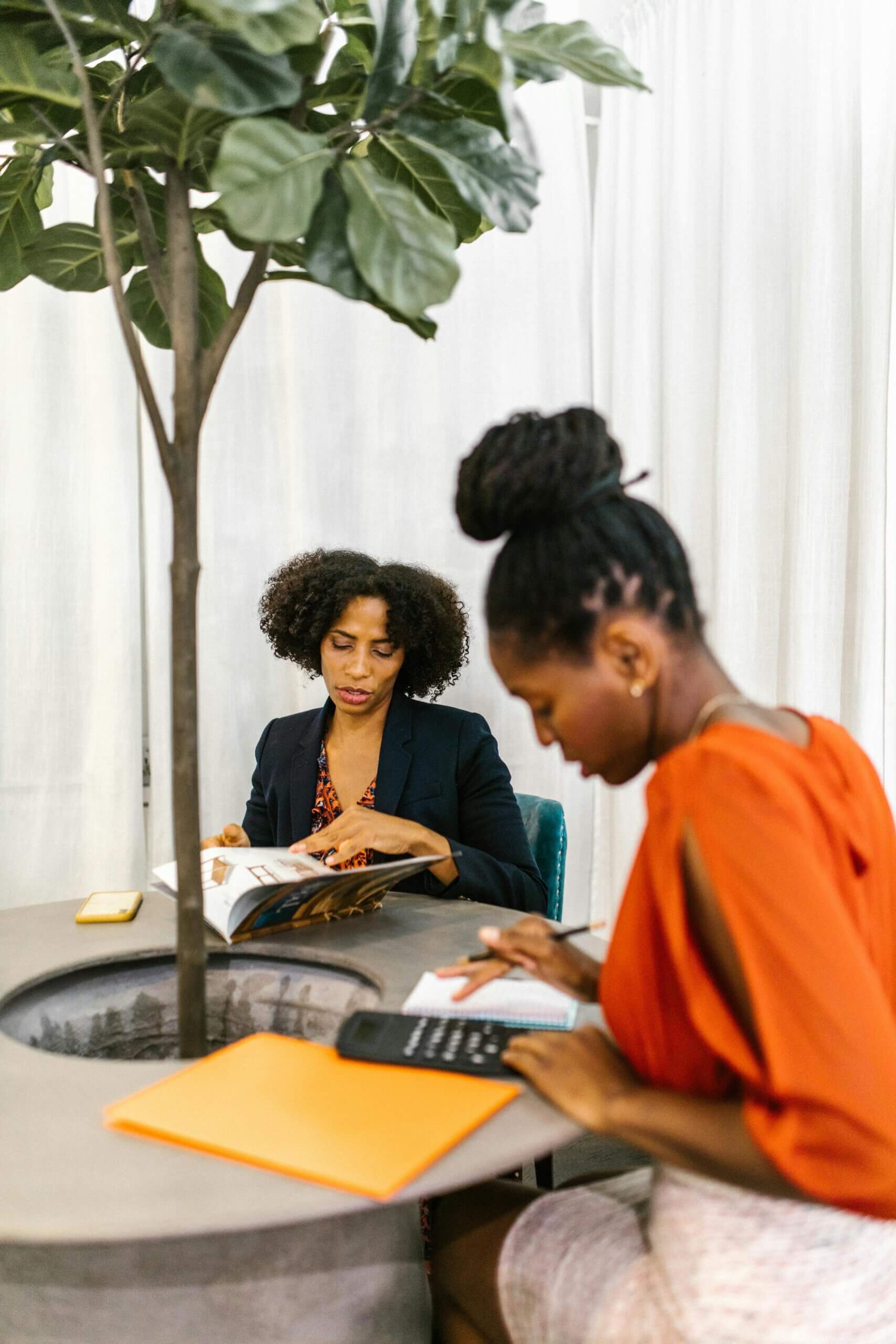 About Two African American women collaborate in a contemporary office setting.